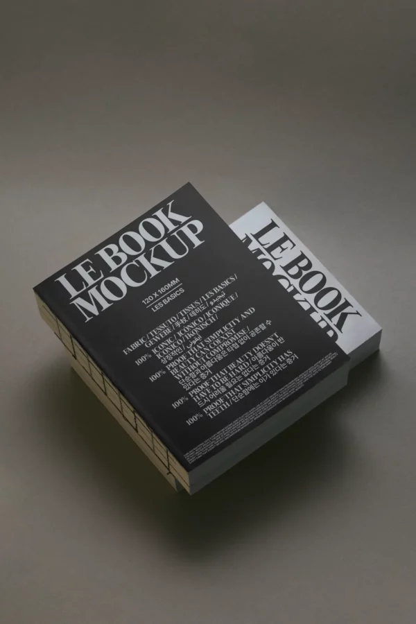Two thick books are stacked on a gray surface. The top book has a black cover and the bottom one has a white cover. Both display the large text LE BOOK MOCKUP on the front with additional smaller text underneath.