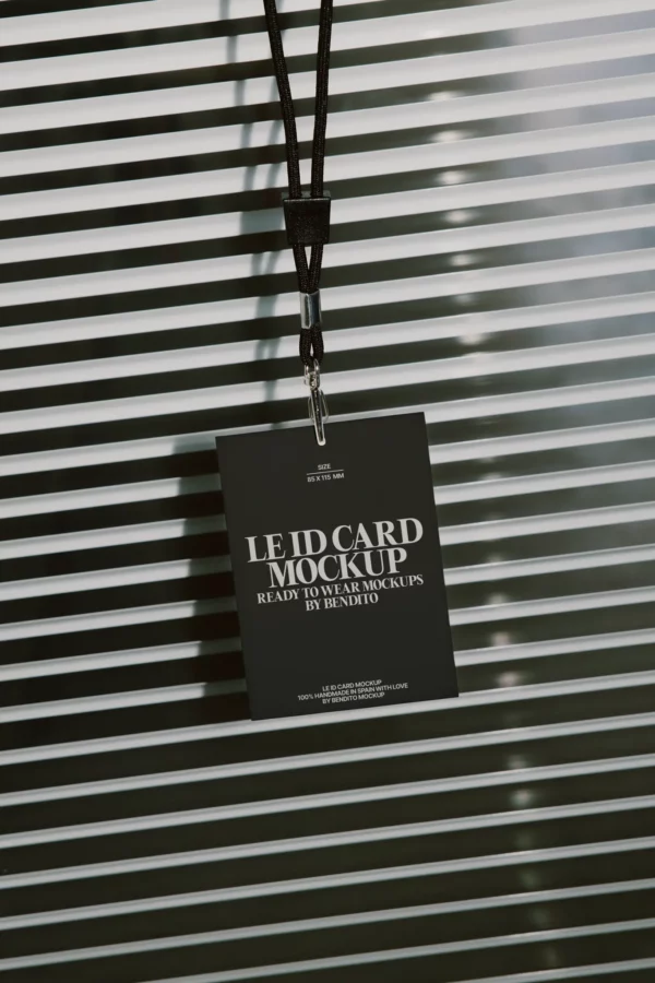 A black lanyard holds a dark ID card mockup with white text, hanging in front of horizontal metal blinds with soft light and shadow stripes in the background.