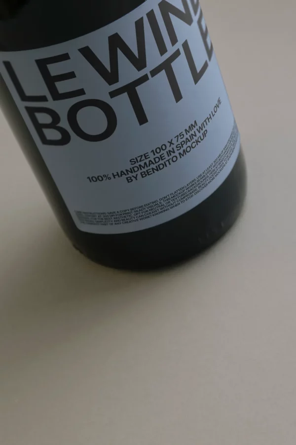 A close-up of a wine bottle with a minimalist gray label that reads “LE WINE BOTTLE” and details about the size, handmade origin in Spain, and “Bendito Mockup.” The bottle rests on a plain, light-colored surface.