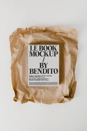 A book mockup with a minimalist cover reading LE BOOK MOCKUP / BY BENDITO sits on a crumpled sheet of brown kraft paper atop a white surface.