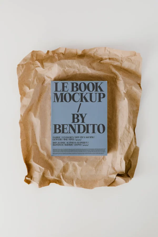 A book with a blue-gray cover titled LE BOOK MOCKUP / BY BENDITO rests on crumpled brown paper against a plain white background.