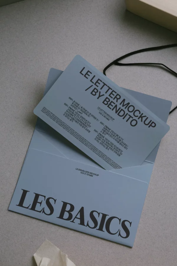 A blue envelope labeled LES BASICS with a matching letter partially pulled out, titled LE LETTER MOCKUP / BY BENDITO, placed on a grey surface. A black string is attached to the letter.
