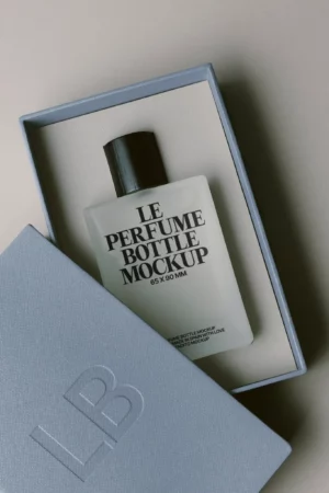 A frosted glass perfume bottle labeled Le Perfume Bottle Mockup 65x90mm rests in a light blue box, with the lid partially open and embossed with the initials LB.