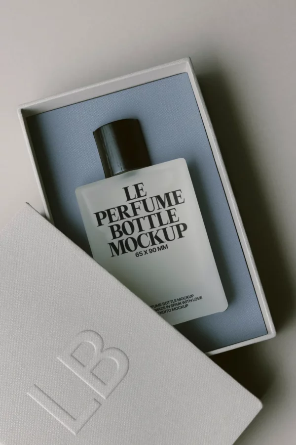 A rectangular perfume bottle labeled Le Perfume Bottle Mockup 65 x 90 mm sits in a cushioned box, partially covered by a white lid embossed with the letters LB.