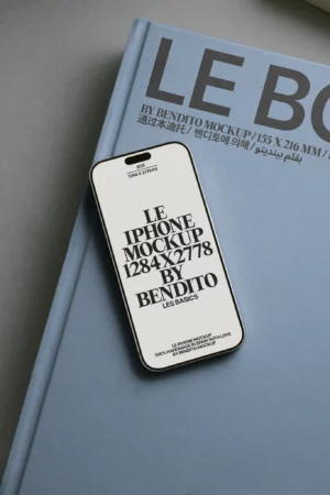 A smartphone displaying a mockup text rests on a large blue hardcover book with multilingual text on the cover. The phone screen shows LE IPHONE MOCKUP 1284x2778 BY BENDITO in bold, black typography.
