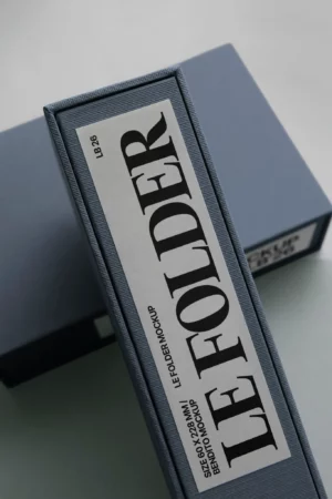 A close-up of a blue binder with a white label on its spine that reads LE FOLDER in large black letters, along with smaller text below and above it. Another binder is partially visible in the background.