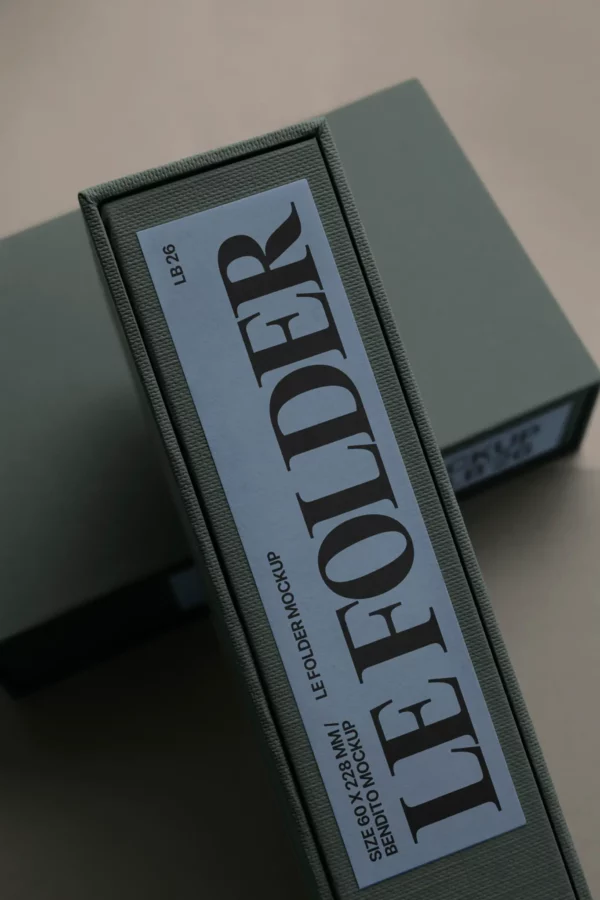 A close-up of a green binder with a large label on the spine reading “LE FOLDER” in bold letters, placed on a tabletop with another similar binder partially visible in the background.