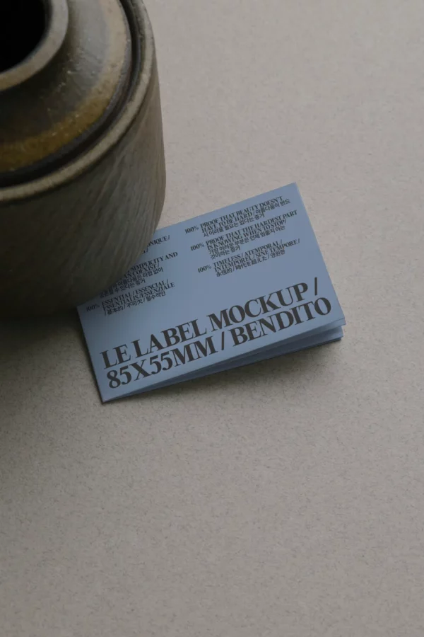 A stack of blue business cards partially covered by a ceramic vase on a beige surface. The top card reads LE LABEL MOCKUP / 85X55MM / BENDITO in large black letters.