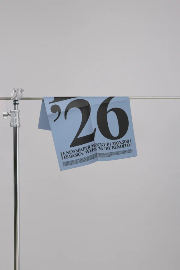 A blue newspaper with large black text reading 26 hangs over a metal rod against a plain grey background. Smaller text appears below the large numbers.