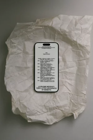 A smartphone with a mockup screen displaying text lies on crumpled, light-colored parchment paper against a neutral background. The phones screen shows specifications and design credits.