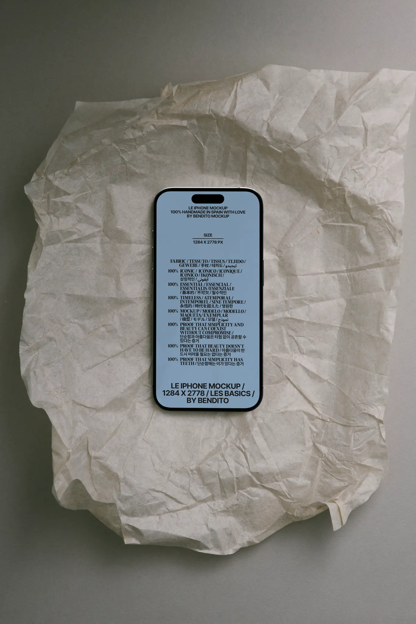 A smartphone with a blue screen displaying text is placed on crumpled white parchment paper atop a gray surface. The phone screen features a mockup template with various font styles and sample text.