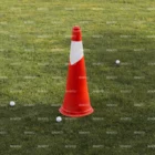 A single orange traffic cone with a white stripe stands on green grass, surrounded by a few scattered white golf balls.
