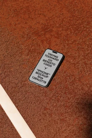 A smartphone with a mockup screen displaying text lies on a brown textured surface next to a light-colored line. The phones screen includes placeholder text about an iPhone mockup and its size.