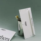 A silver cup holds a bamboo toothbrush and a partially visible envelope, alongside another envelope labeled The Bathers in large text. This mockup is set against a muted green background for a modern, minimalist look.