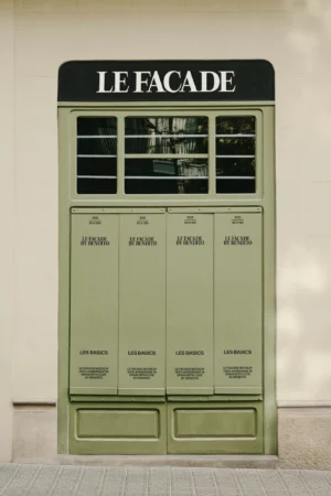 A green facade designed to look like a storefront with the words LE FACADE on top and LES BASICS on the lower panels, featuring over four compartment-like sections and rectangular windows above.
