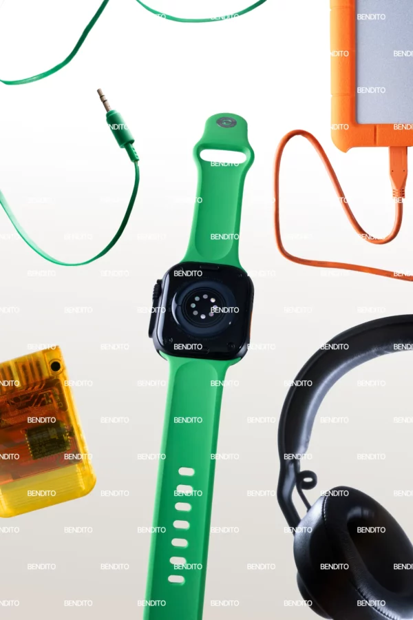A green smartwatch with a black face is centered among electronic accessories, including headphones, an orange hard drive, a green audio cable, and a translucent orange device, all on a white background.