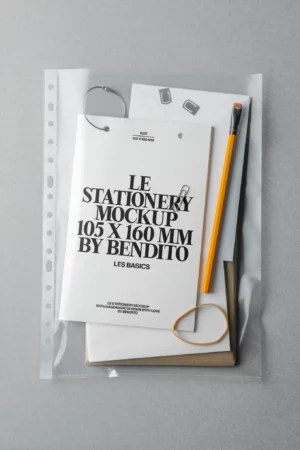 A clear plastic folder containing a notepad with LE STATIONERY MOCKUP 105 X 160 MM BY BENDITO printed on the cover, a yellow pencil, rubber band, metal ring, and black paper clips, all on a gray surface.